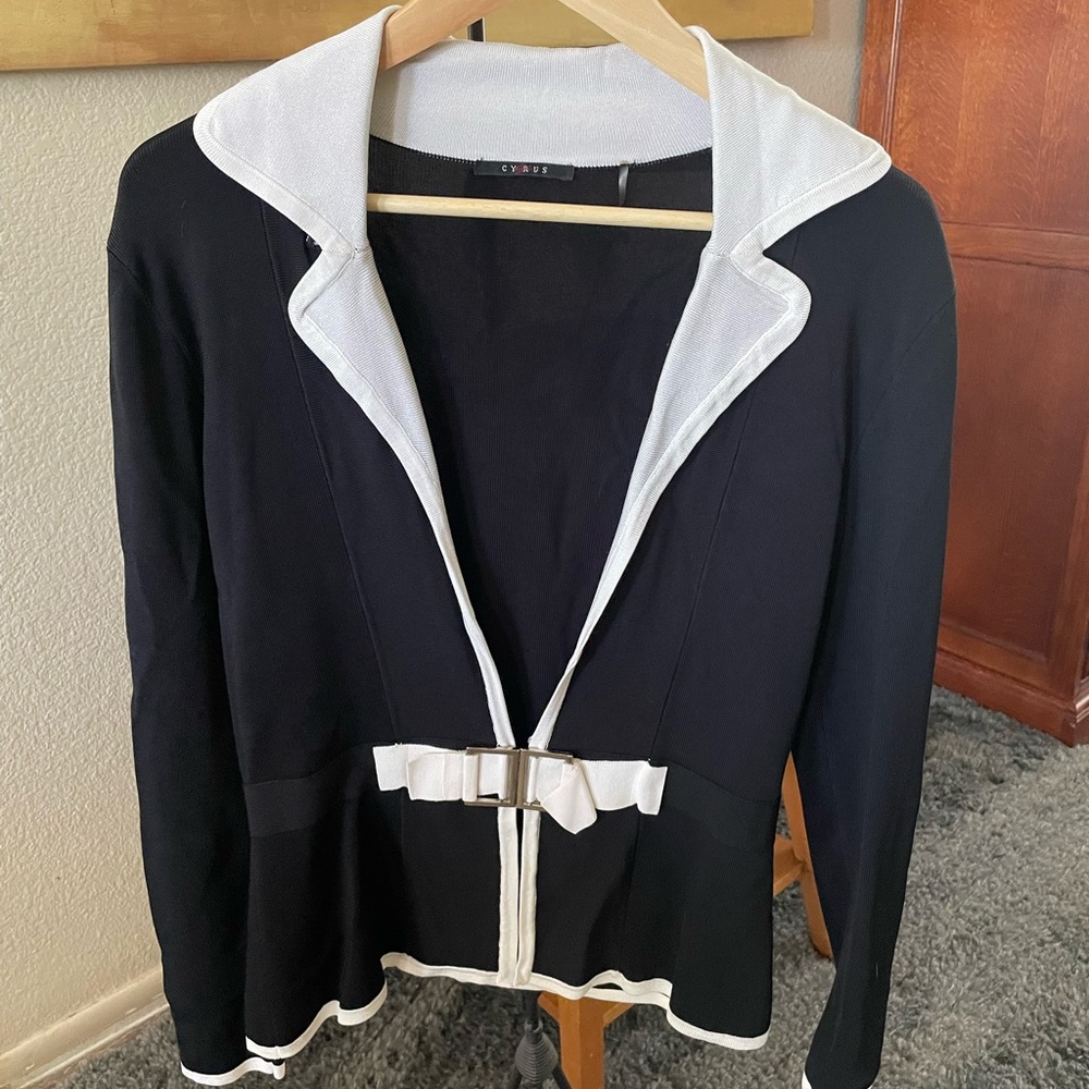 Cyrus, black long sleeve jacket with white trim and clasped belt.